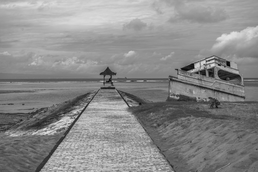 A brick path with small pagoda-like structure at the end, reaching out to the ocean