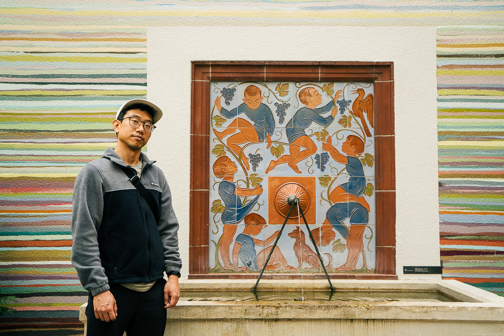 D standing next to a fountain with cool, rainbow-striped walls and beautiful mosaics