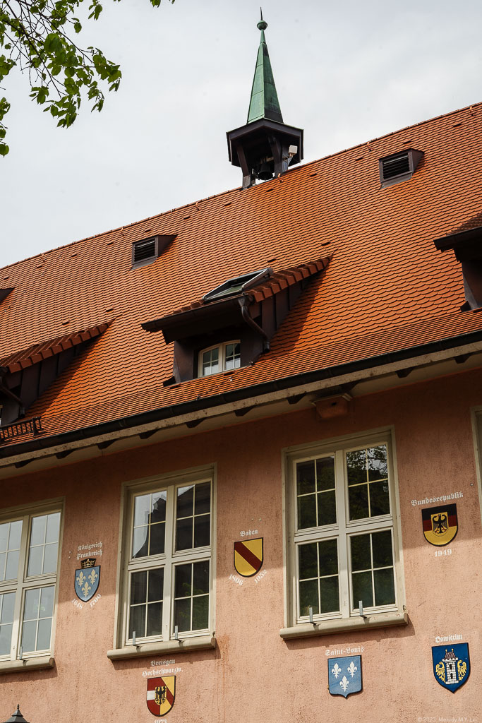 A pink building on the side of the church with coats of arms fo German states.