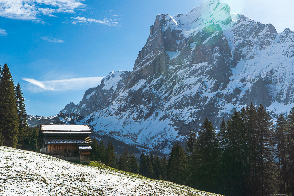 A barn on the hillside and a dusting of snow on green grass