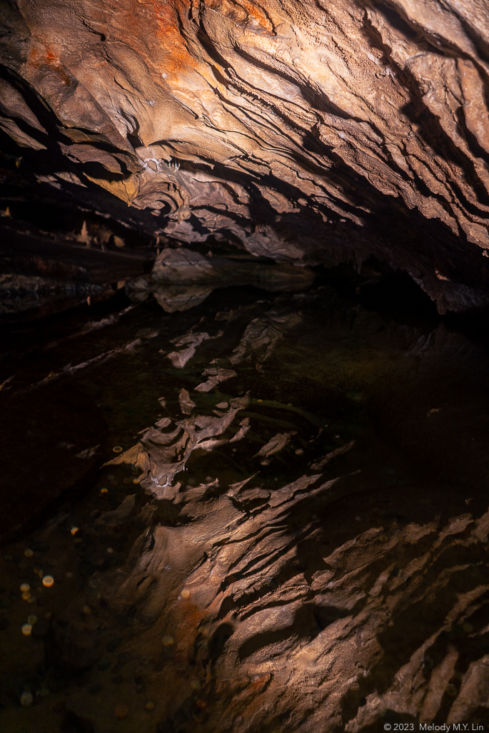 Weird ripples form along the cave ceiling, reflected by a large pond